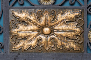 Close-up of an ornate golden decorative element mounted on a dark wrought iron background, showcasing craftsmanship, luxury texture and antique design style