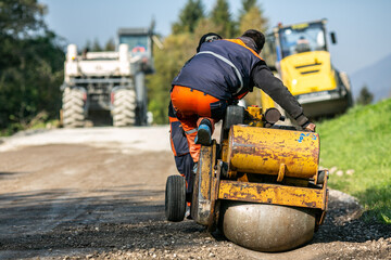 Construction worker using small motorized machine to create drainage groove along road edge at construction site