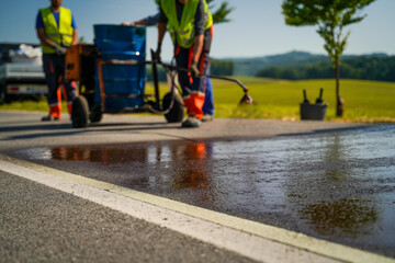 Low angle close-up of construction worker spraying fresh coat of liquid bitumen on the road repair site showing texture and reflection