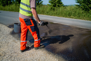 Road repair worker distributing gravel onto fresh bitumen coating on a renovated road section