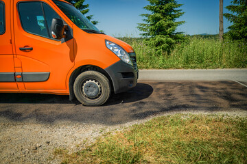 Fototapeta premium Close-up of asphalt road section repaired with liquid bitumen coating and gravel spread on top, with a vehicle driving across it