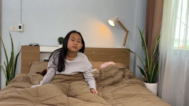 Wake up concept, Happy young Asian Thai Little girl stretching on her bed in the morning, Wearing white pajamas
