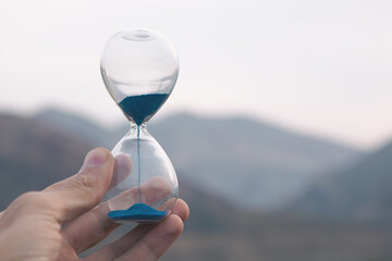 hand holding glass hourglass on blurred background