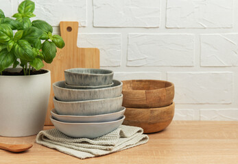 Kitchen table setting featuring stacked bowls, fresh basil, and cutting board