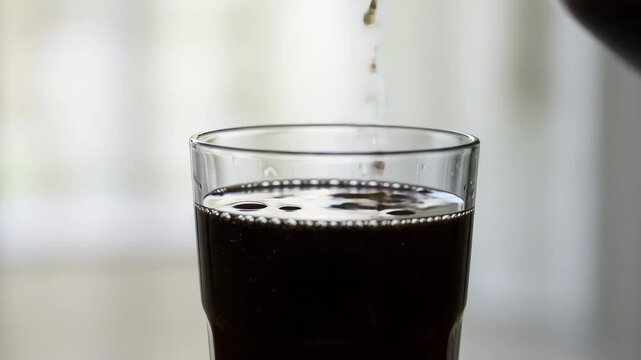 Pouring cola into a glass. Refreshing beverage with bubbles. Perfect for illustrating drinks, refreshment, or a treat.