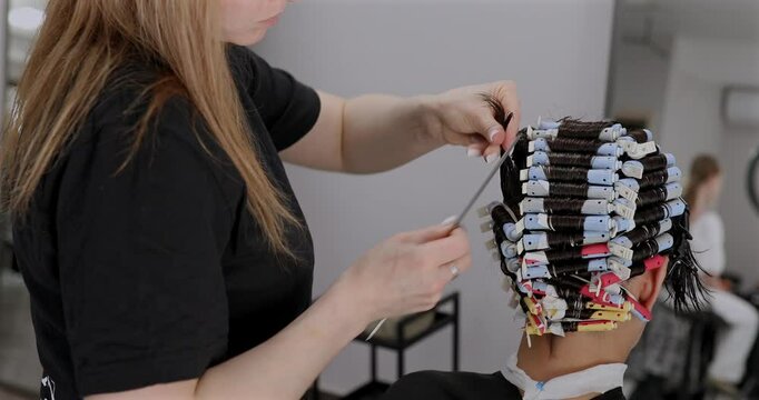 Professional hairdresser working with client, closeup. Hairdresser winding perm rods. Hair curlers.