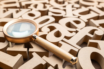 A magnifying glass placed on the group of the wooden English alphabets, find the word to communicate, glossary concept