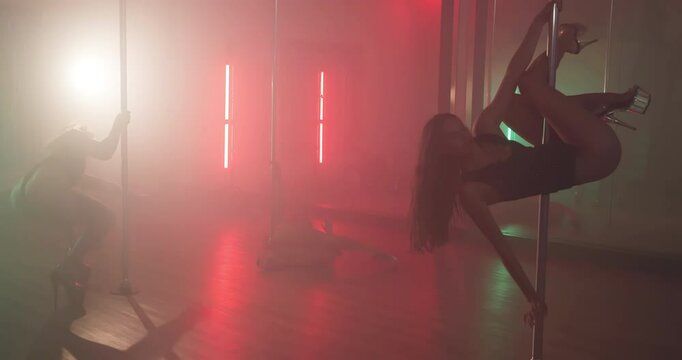 Women, dancing and pole in studio with neon lights, choreography and practice show. Burlesque, people and exotic dancer group at mirror for performance, spinning and smoke for aesthetic in spotlight