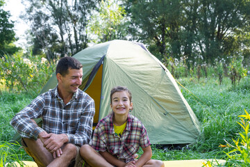 Portrait of a happy family dad and daughter sitting in the morning near the outdoor camping tent, camping, family hiking trip