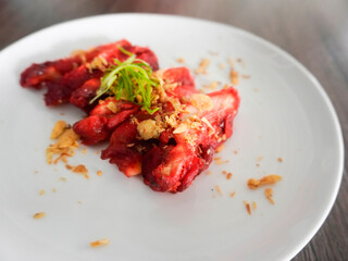 A delicious Chinese dish, Char Siu Chicken or Roasted Char Siu Chicken or Char Siew, a bright red chicken made from red yeast rice. It is served in a white plate on a wooden table. Selective focus