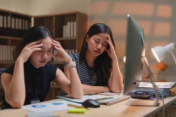 Two young asian businesswomen are having a headache and feeling tired from working on a computer in...