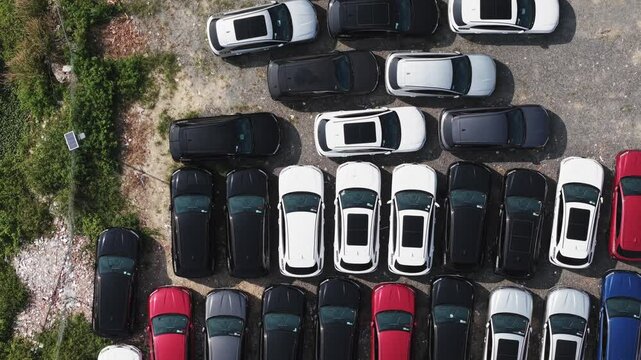 Forward-moving drone shot over a parking lot filled with abandoned cars. The camera glides steadily above the rows of dusty, unused vehicles in a forgotten urban space.