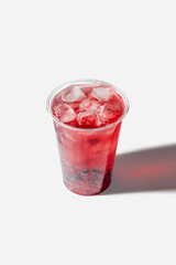 a plastic cup with bright red lemonade, lots of ice and juice balls. A cool summer drink with ice, isolated on a white background.