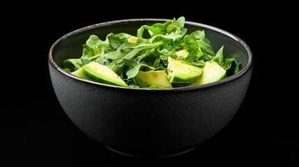 A dark bowl filled with fresh arugula and avocado, showcasing vibrant greens against a black background.