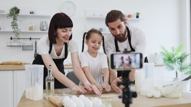 Caucasian family with parents and child filming baking tutorial, creating culinary vlog content.