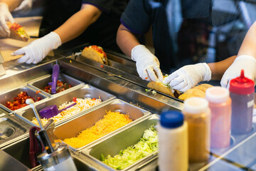 Team of Workers Preparing Mexican Tacos with Fresh Ingredients at Fast Food Restaurant Counter