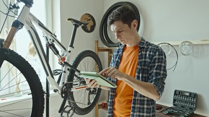 A male bicycle mechanic in the repair shop disassembles a mountain bike and repairs it. Maintenance concept, preparation for the new season - Powered by Adobe