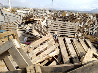 Wood waste collected for recycling outdoors in the Waste Center area. Mixed wood waste. Iron structure warehouse and mountains in the background of wood waste