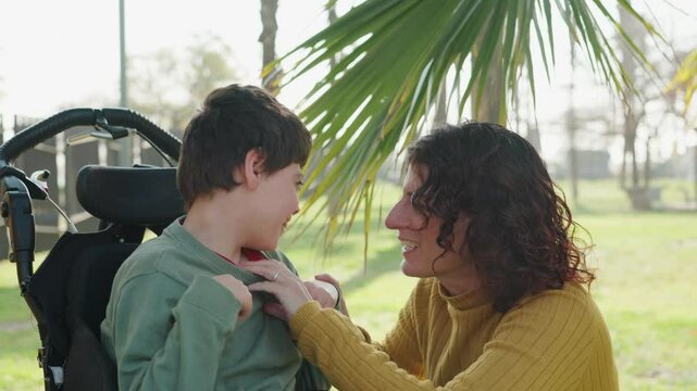 Mother tickling disabled son in wheelchair outdoors