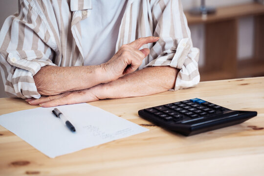 elderly woman sitting at home at the desk with calculator and calculating finances or taxes. Senior retired woman counting income and profit. Pension calculation concept