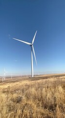 A photograph of white wind turbines against the blue sky, with one in the foreground and others in the background
