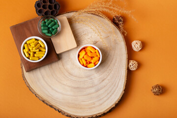 Many colored vitamin pills in small bowls from above on wooden desk on orange background. Rustic composition with food supplements. Dietary supplements and healthy lifestyle. Vitamins and minerals.