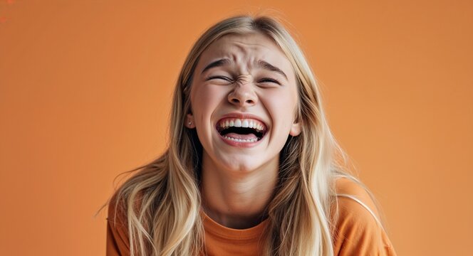 blonde teen girl on orange plain bright background happy laughing hysterical looking at camera portrait banner with copy space ad concept marketing