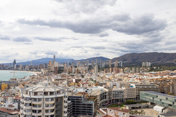 Naklejka premium Aerial photo of the Spanish town of Benidorm in Spain showing the old town of the city with the beach known as Platja de Ponent or West Beach Promenade in background as well as mountains and clouds