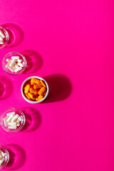 Dietary supplements, vitamins and minerals pills in small plates from above on a pink background.