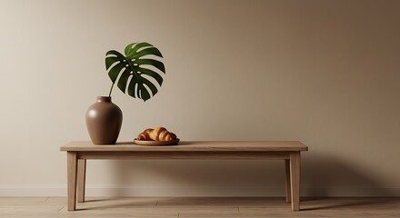 A serene minimalist scene of a monstera leaf in a brown vase and croissants on a light wood table against a warm beige wall.