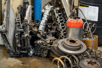 Garage corner with pile of used vehicle parts including brake discs, engine components and coil...