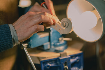In Cremona, Italy, a luthier sculpts a violin scroll under warm lamplight, showcasing detailed handcrafting with a chisel, a blue vise holding the wood firmly on a wooden workbench surface.