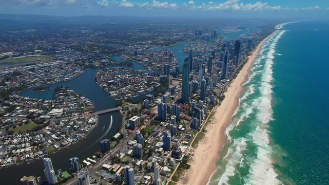 Aerial panorama of Gold Coast showcasing endless sandy beaches, the ocean, towering skyscrapers, and low-rise suburbs. Bright summer day with vibrant colors and stunning coastal views.