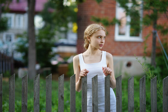 Girl in a white dress standing by a fence outdoors