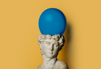 antique statue of a young man on a yellow background with a blue balloon
