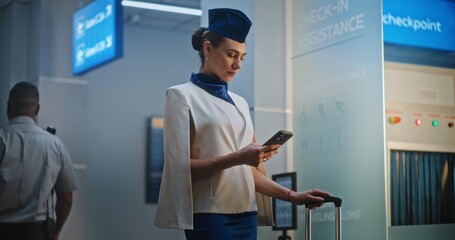 Beautiful Stewardess in Elegant Uniform Scrolls Phone, Waits for Boarding Flight. Professional Cabin Crew Member in Crowded International Airport Terminal Full off People in Background. Medium Shot.
