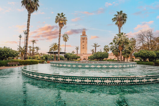 The majestic Koutoubia Mosque rises above a serene fountain in Marrakech, Morocco, bathed in the warm glow of the setting sun