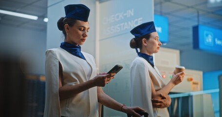 Two Beautiful Flight Attendants in Elegant Uniforms Talking, Waiting for Commercial Flight. One...