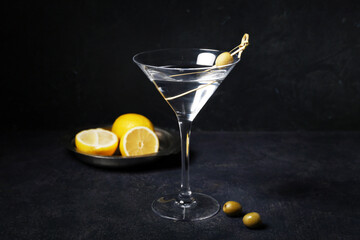 Glass of tasty martini with olives and lemon on dark background
