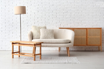Cozy white sofa, table and cabinet near brick wall