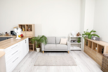 Interior of light living room with grey sofa and modern fan on counter