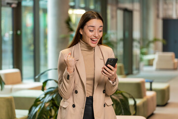 Happy amazed young businesswoman girl working on smartphone shocked by sudden victory game winning...
