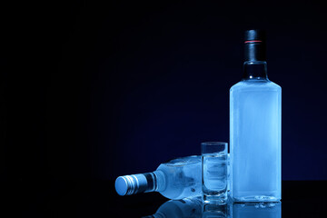 Bottles and shot of cold vodka on black background