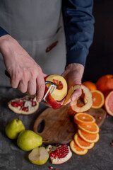 men's hands peel an apple using a special peeling knife, with other fruits lying in the background.