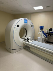 A large MRI machine is in a hospital room. The machine is white and has a blue screen. The room is...