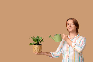 Smiling woman watering potted houseplant on beige background