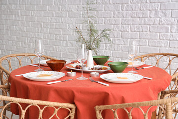 Autumn table setting with burning candles and dry leaves in light room