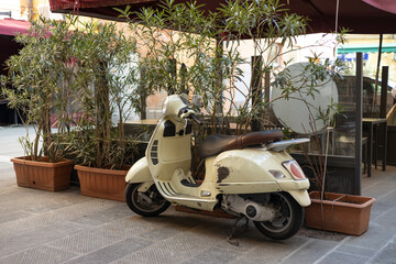 White retro-style scooter on town street. Motor standing at the empty street of old Italian town