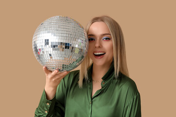 Beautiful young woman with disco ball on brown background