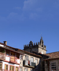 Obraz premium Medieval clock tower in an old square in the city of Guimarães in Portugal, Largo da Oliveira, Church of Our Lady of Oliveira, facade of old buildings with clothes drying on the balconies, typical